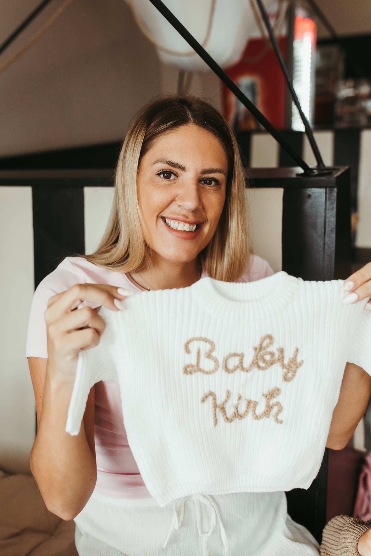 Woman holding a white baby romper with 'Baby Kirk' embroidered on it.