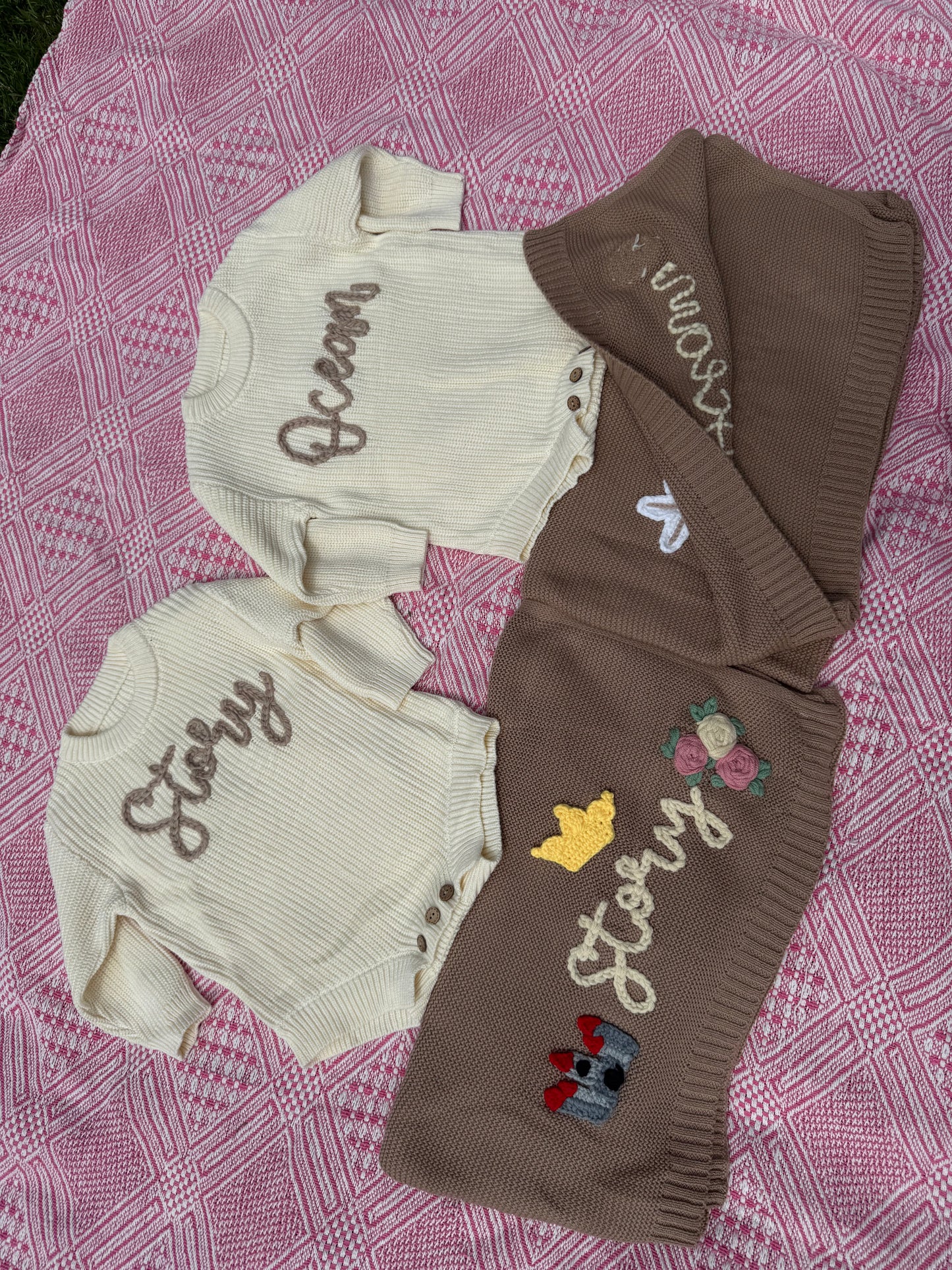 Baby rompers and matching blankets with embroidered designs on a pink textured fabric background